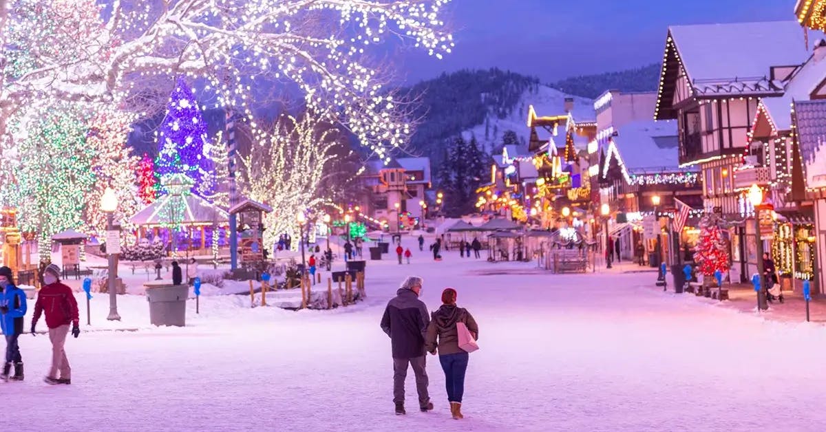 A snow-covered street featuring Leavenworth, Washington’s Christmastown Village of Lights at night with buildings covered in Christmas Lights and Bavarian-styled buildings covered in Christmas decorations