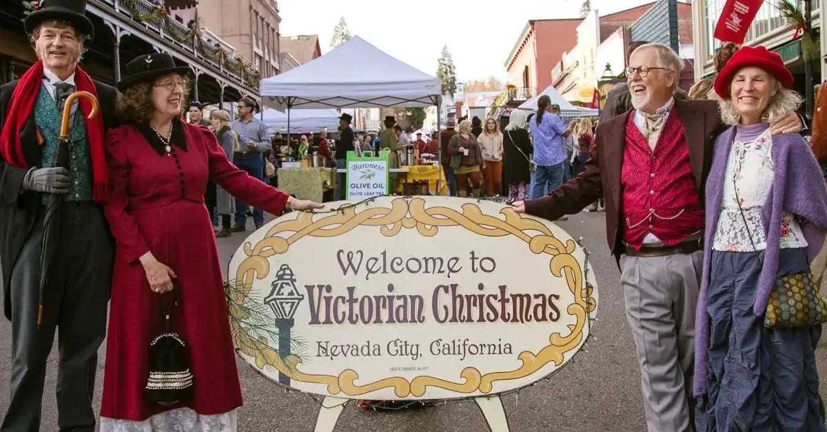 Two couples in Victorian dress posing next to the “Welcome to Victorian Christmas” sign in Nevada City, CA