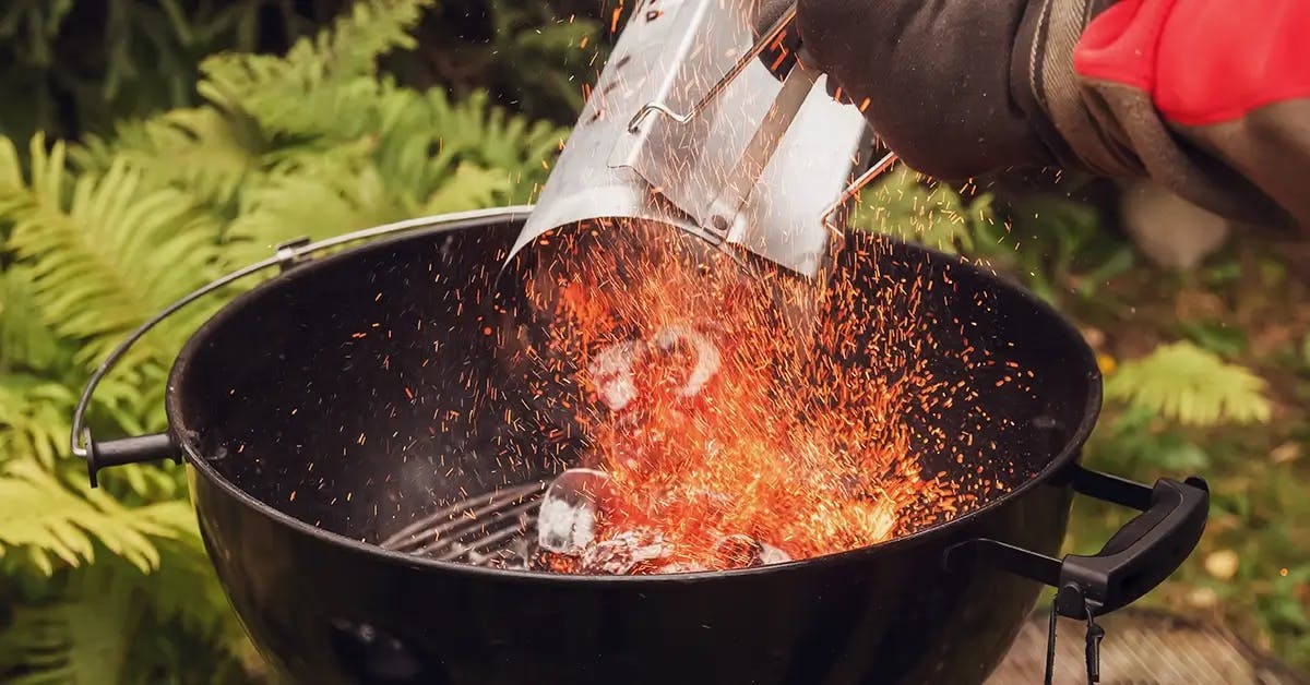 Hand adding hot coals from a chimney starter to a charcoal barbecue.