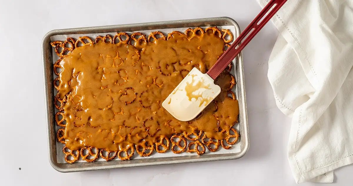 Spreading melted toffee over a layer of pretzels on a baking sheet, ready to make Christmas Crack.