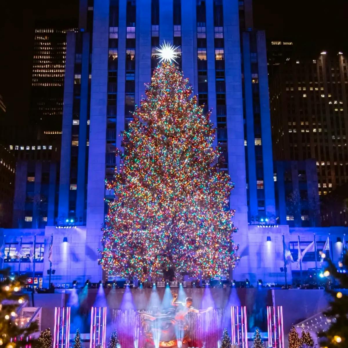 Rockefeller Center Christmas Tree with lights at night with the New York City buildings behind.