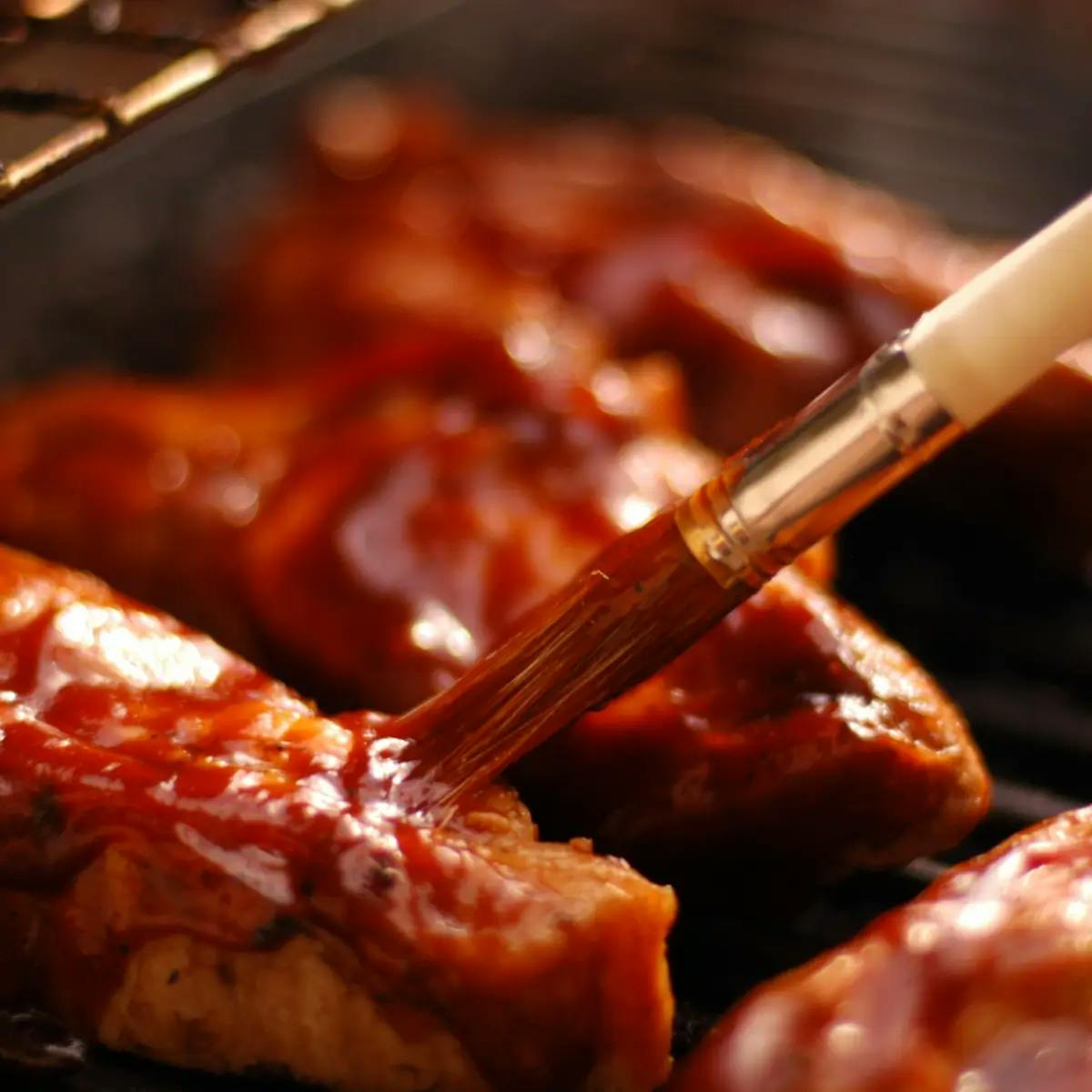 Brush applying sauce or glaze to meat on a barbecue grill.