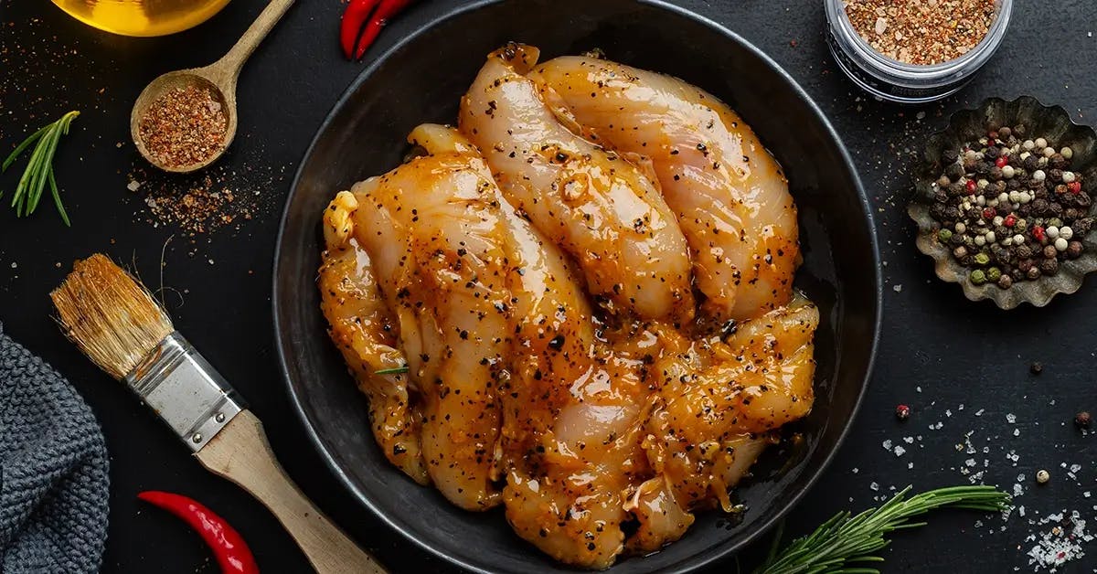 Pieces of chicken marinating in a bowl before a backyard barbecue.