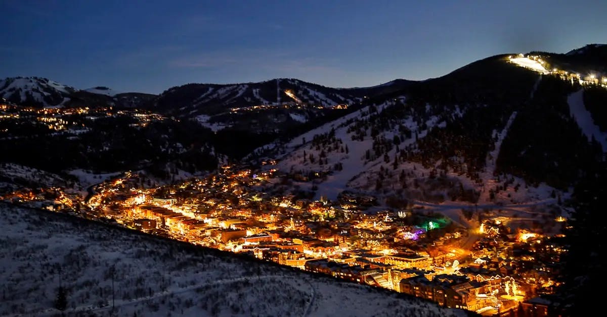 Park City, UT at night, nestled between snow-covered mountains and lit with Christmas lights.
