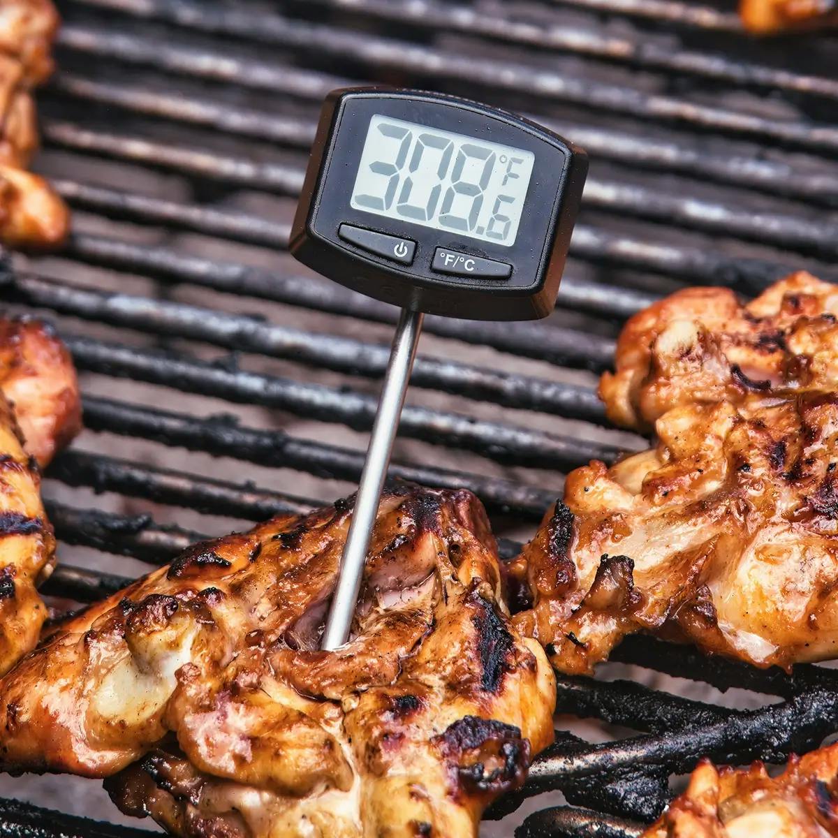 Digital thermometer in a piece of chicken on a charcoal grill.