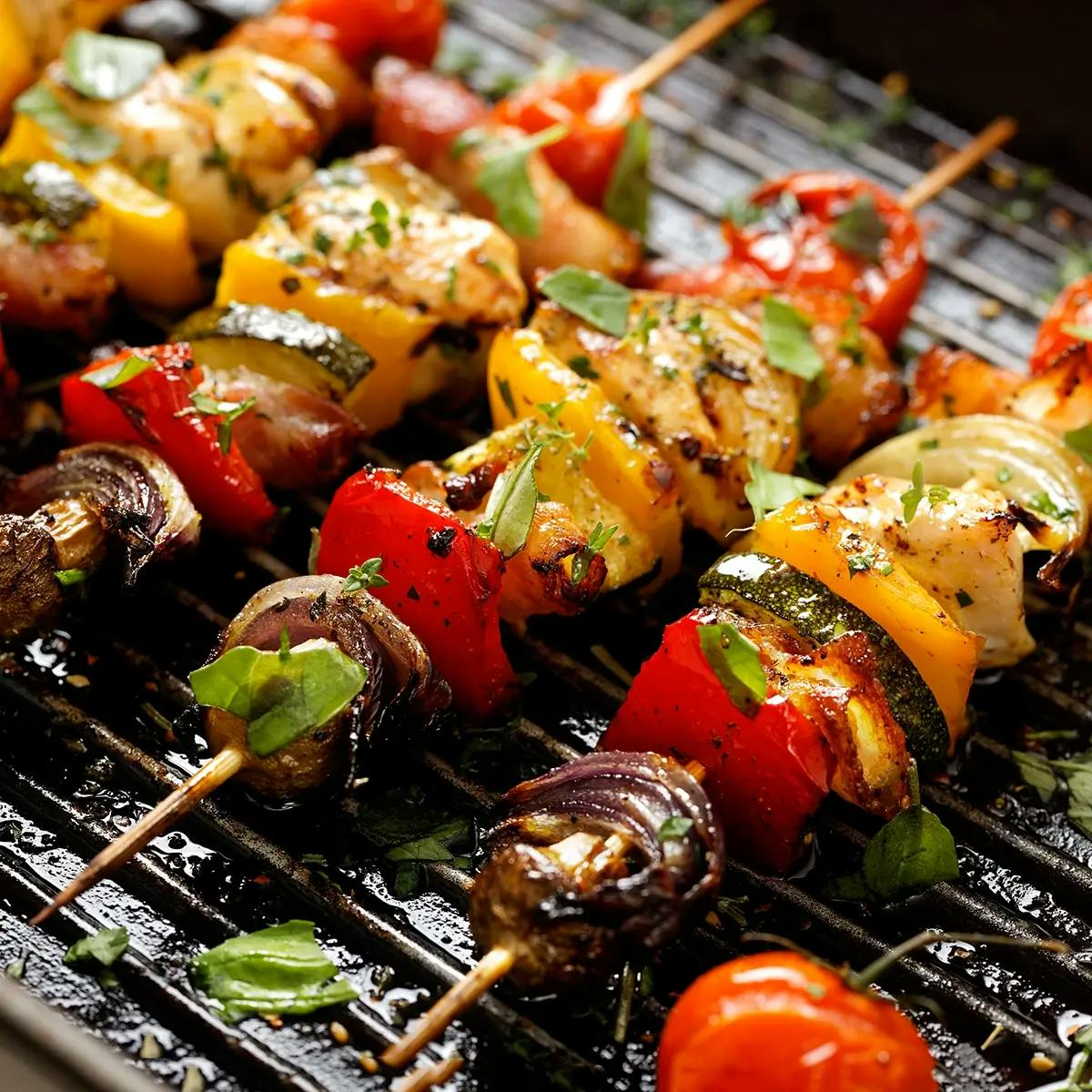 Wooden skewers loaded with vegetables on a charcoal grill.