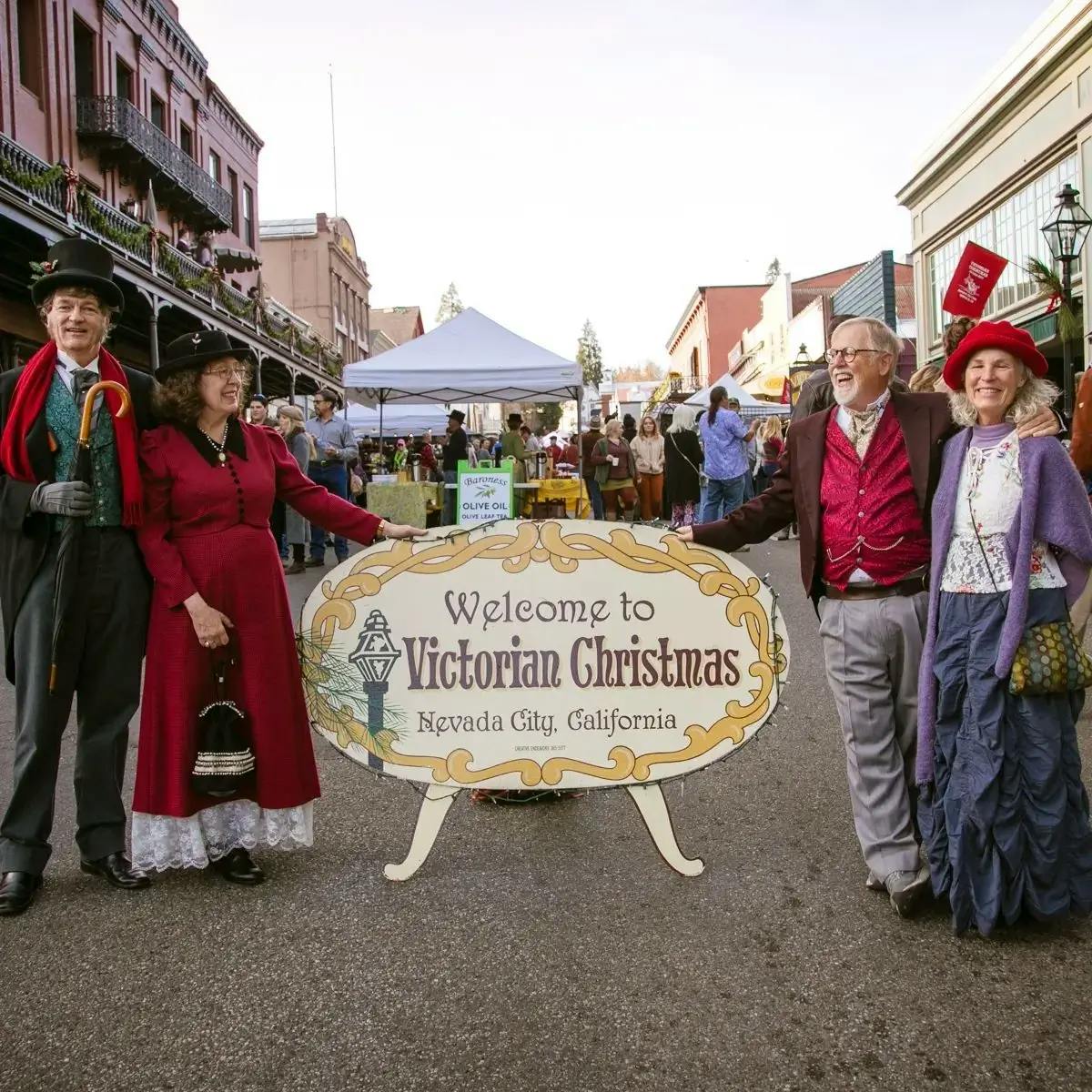 Two couples in Victorian dress posing next to the “Welcome to Victorian Christmas” sign in Nevada City, CA
