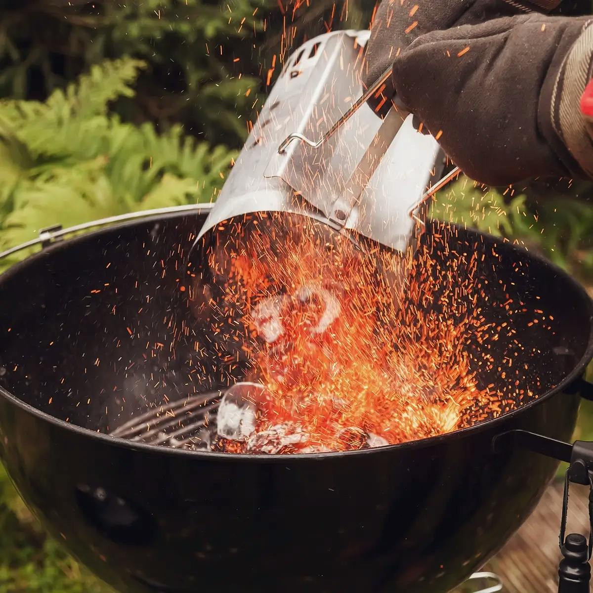 Hand adding hot coals from a chimney starter to a charcoal barbecue.