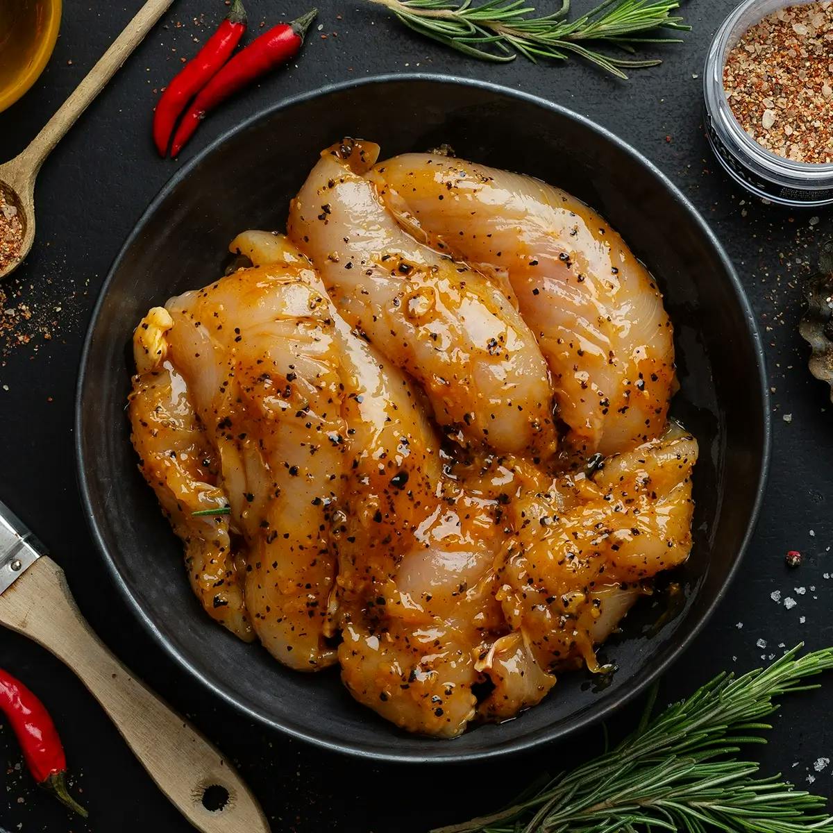 Pieces of chicken marinating in a bowl before a backyard barbecue.