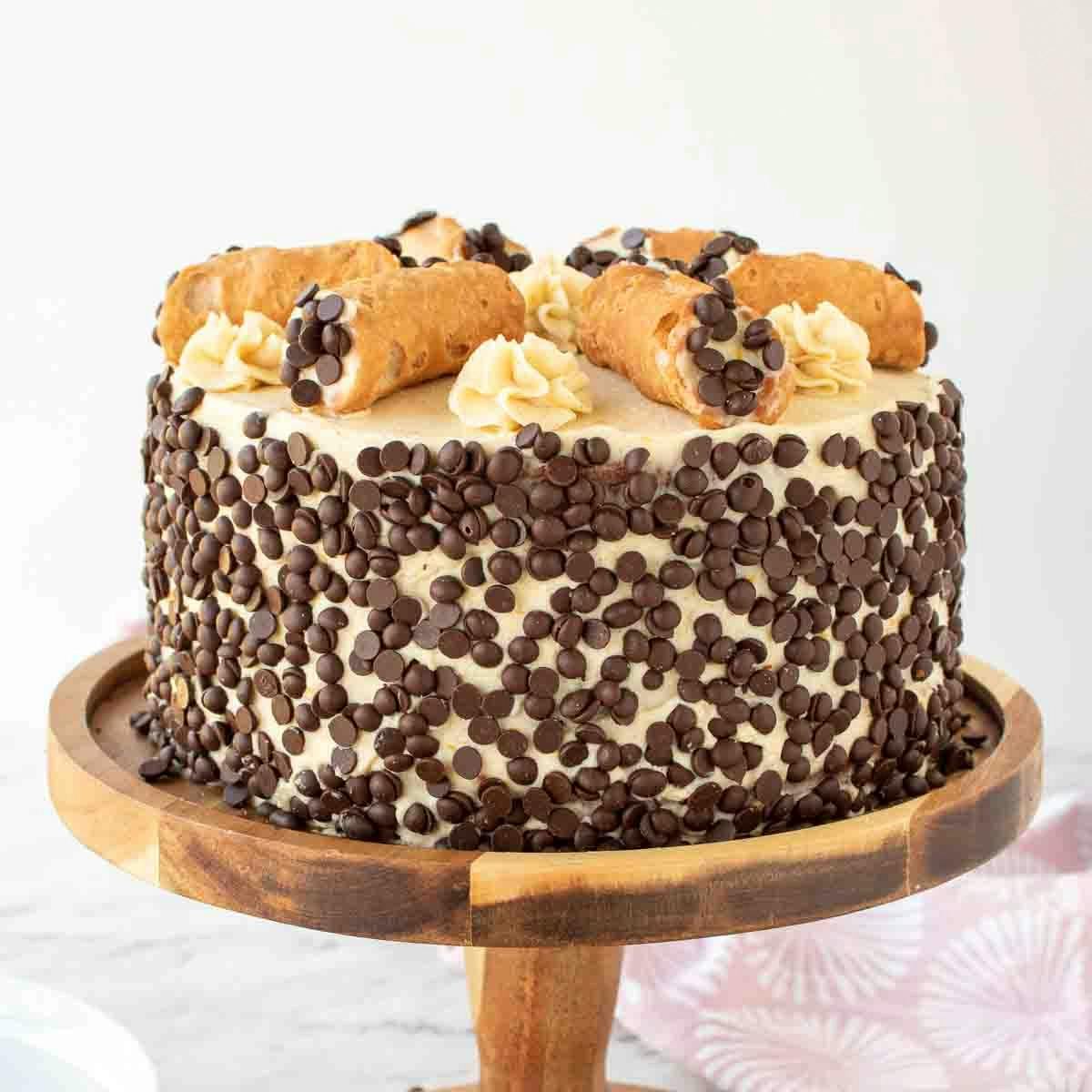 A cannoli cake on a stand for Mother’s Day brunch, studded with chocolate chips and topped with small cannolis.