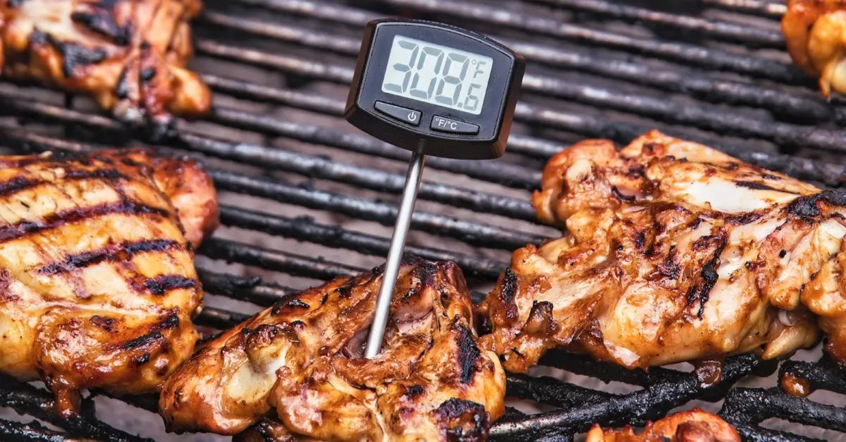 Digital thermometer in a piece of chicken on a charcoal grill.