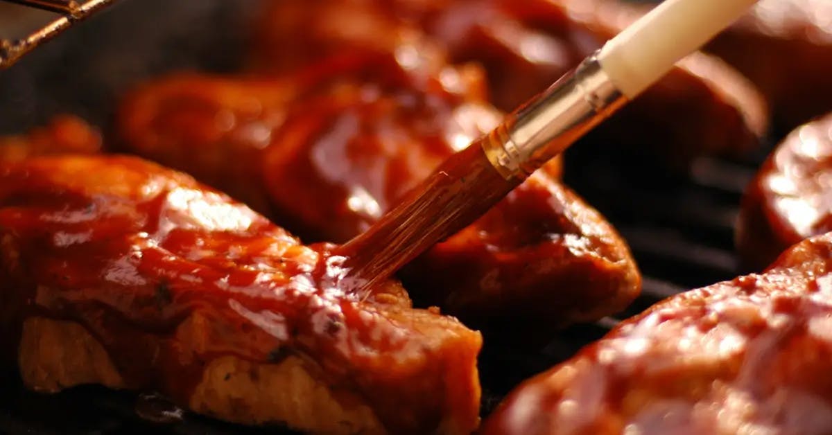 Brush applying sauce or glaze to meat on a barbecue grill.