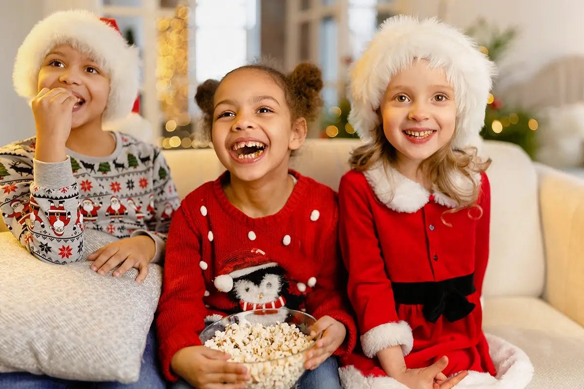 Children sitting on a sofa watching a Christmas in July movie, holding popcorn.