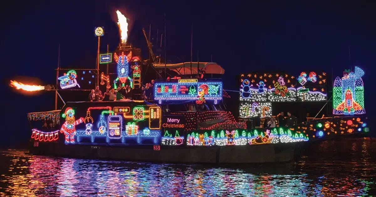 A multi-level boat on the water in the Newport Beach Harbor covered in Christmas lights and decorations