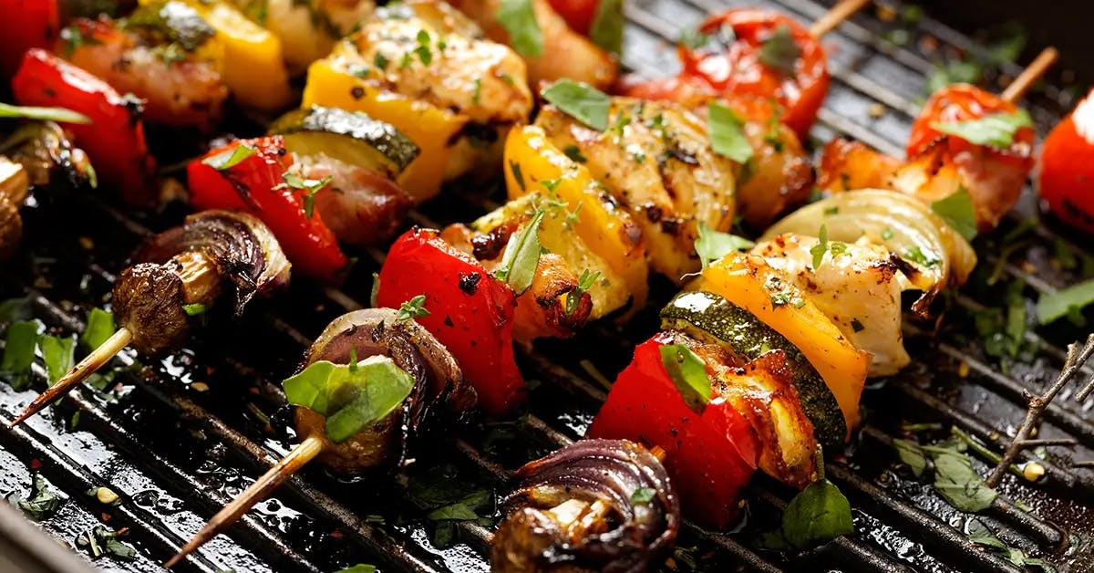 Wooden skewers loaded with vegetables on a charcoal grill.